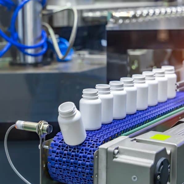 Moving polypropylene white bottles on conveyor belt of automatic liquid filling machine